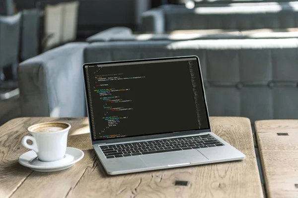 Laptop dengan kode program dan secangkir kopi
